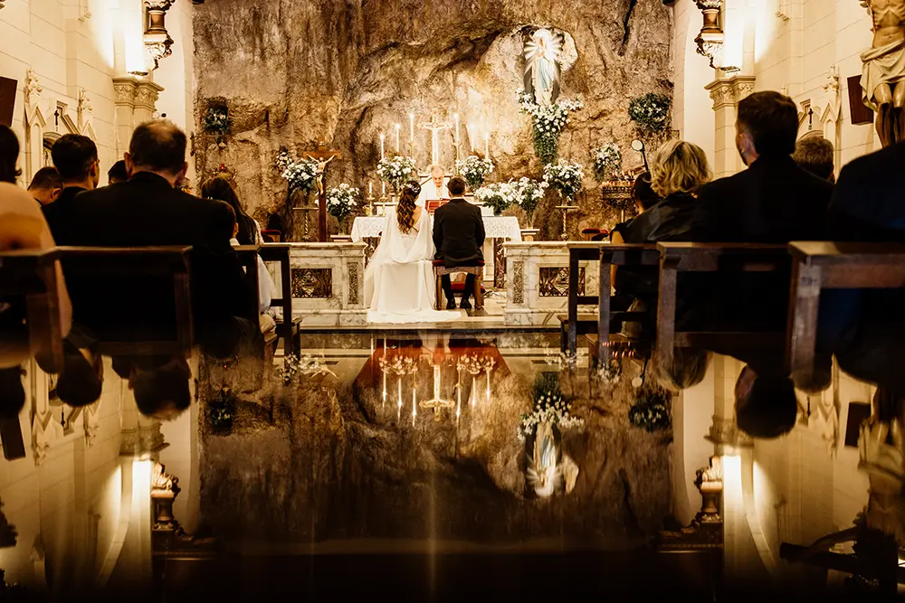 Novios en el altar de espalda con imagen de la gruta en iglesia Lourdes