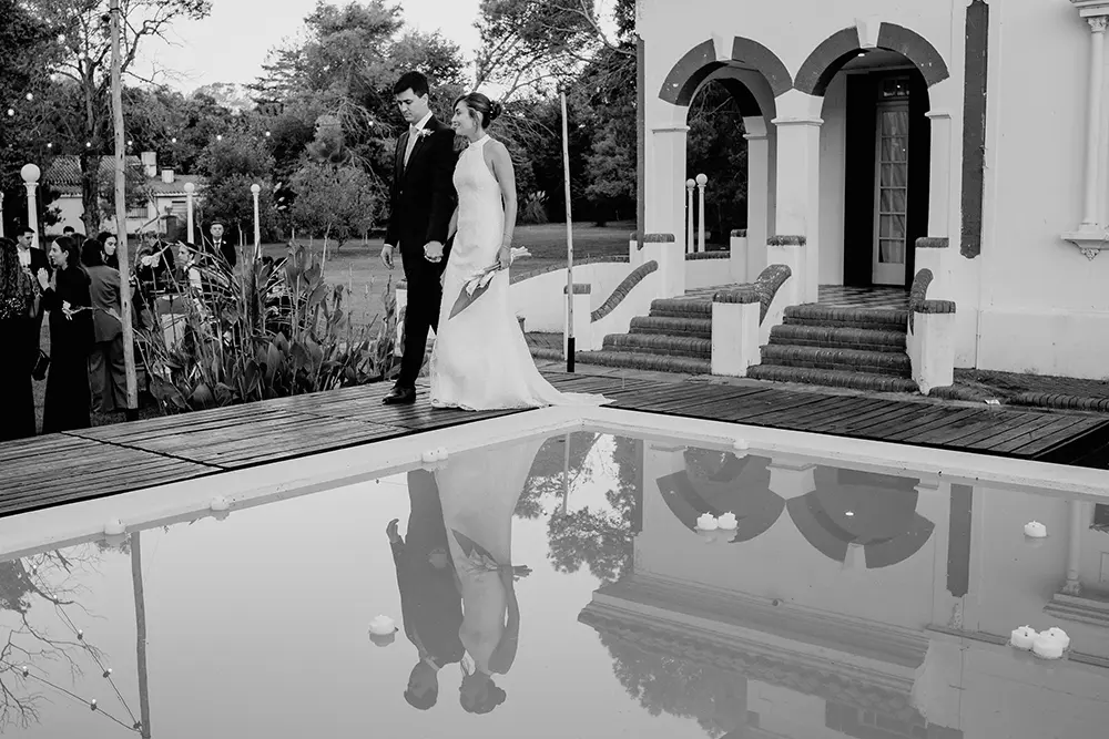 Novios caminan junto a la pileta, se ve el reflejo en el agua